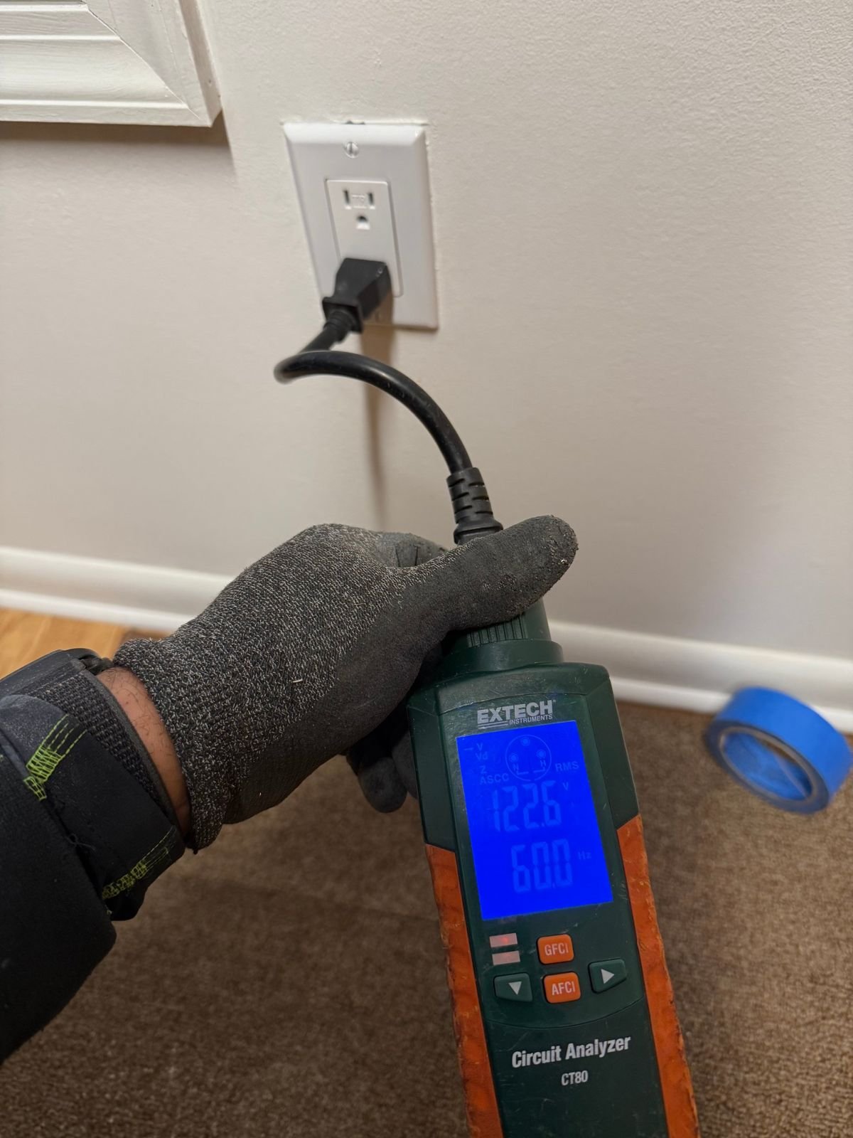 An electrician testing a circuit with an Extech circuit analyzer plugged into a receptacle.