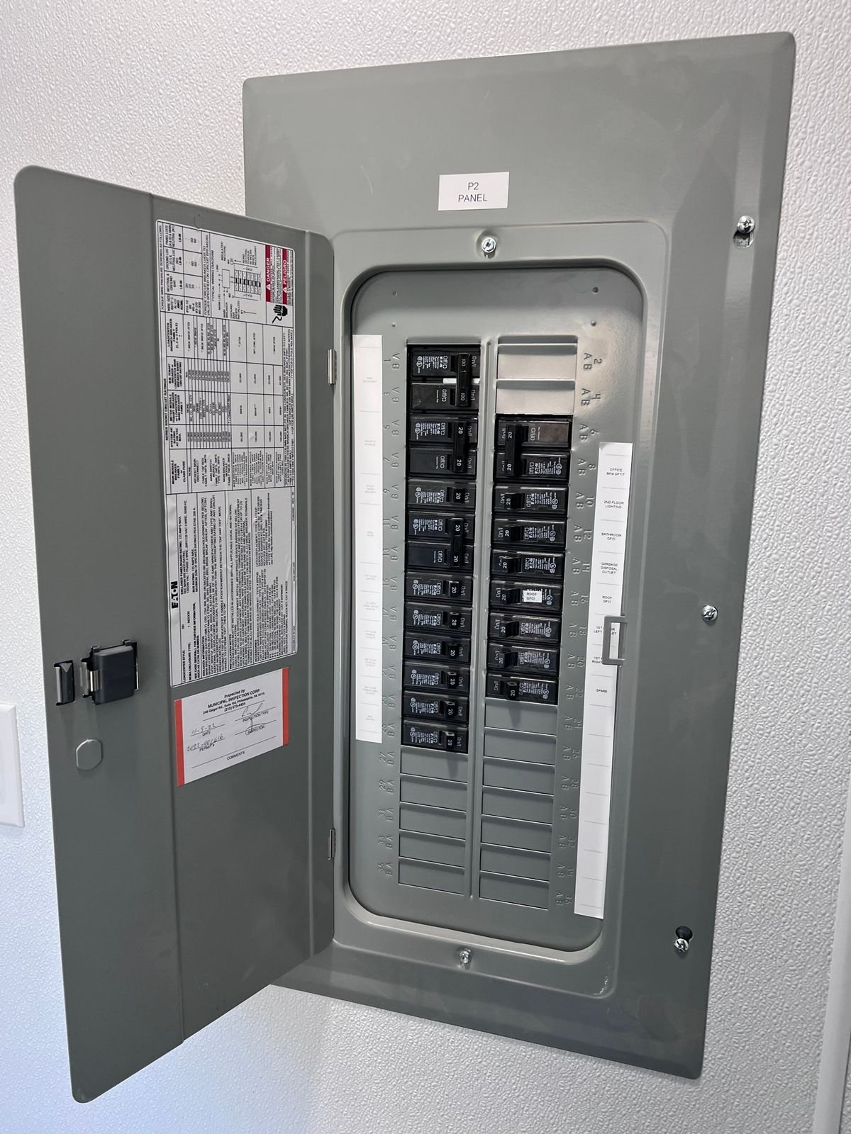 An Eaton panel with every breaker labeled by room and an inspection sticker on the door.
